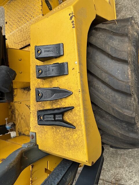 Four black metal clamps arranged on a yellow surface near a large tire.