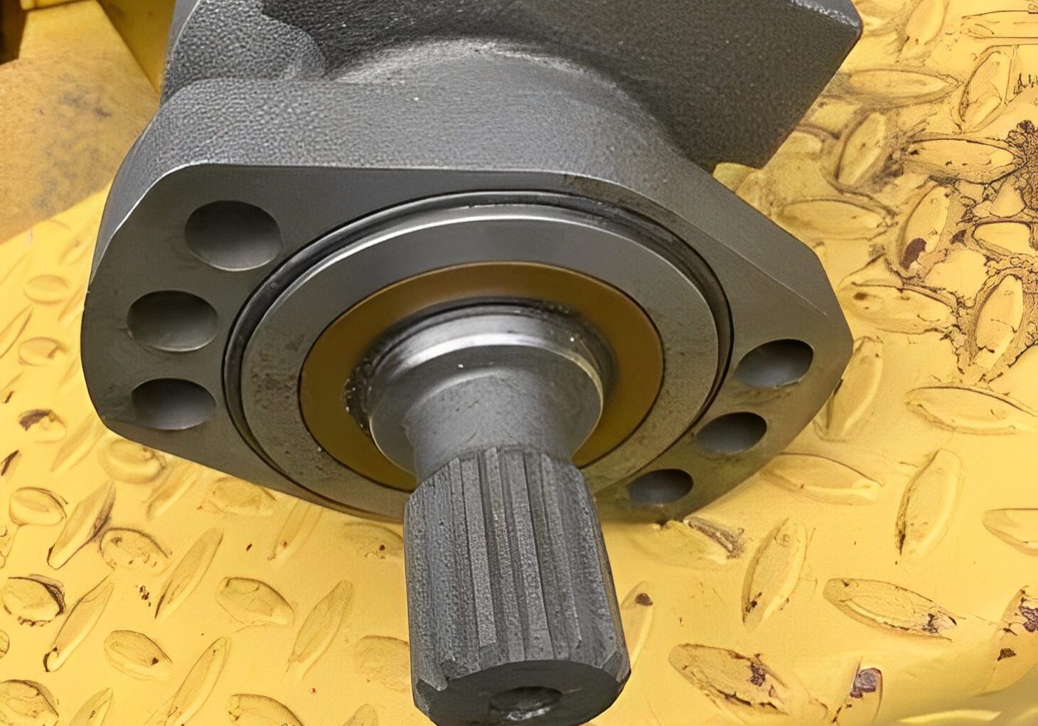 Close-up of a mechanical part with a splined shaft on a yellow surface.
